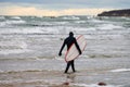 Male surfer in swim suit walking along sea with surfboard Royalty Free Stock Photo