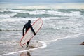 Male surfer in swim suit walking along sea with surfboard