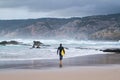 Male surfer walking on a sandy beach towards the ocean carrying a surfboard under his arm. Royalty Free Stock Photo