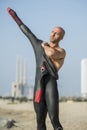 Male swimmer getting ready for swim training in the beach with urban background. Confident man putting on a wetsuit to Royalty Free Stock Photo