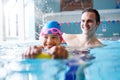 Male Swimming Coach Giving Girl Holding Float One To One Lesson In Pool