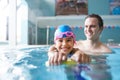 Male Swimming Coach Giving Girl Holding Float One To One Lesson In Pool