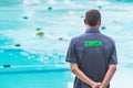 male swimming coach standing by the swimming pool watching swimmers racing by