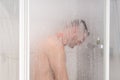 Male taking a shower standing behind transparent misted glass do Royalty Free Stock Photo