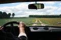 Male tanned hands with a tucked shirt on the steering wheel of a riding car and the road,