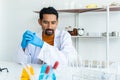 Male teacher in white lab coat with rubber gloves with many laboratory tools on shelves and table. Looking at blue and yellow Royalty Free Stock Photo
