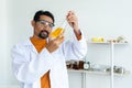 Male teacher in white lab coat with safety glasses looking serious at mixed chemical liquid in bottle and pipette