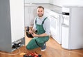 Male technician with clipboard and tools near broken refrigerator