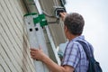 A male technician is doing maintenance work by inspecting and cleaning an outdoor security