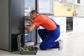 Male technician with screwdriver repairing refrigerator in kitchen Royalty Free Stock Photo