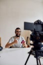 Male technology blogger in glasses showing thumbs up, holding game controller joystick while recording video blog or