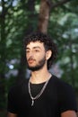 Male teenager with curly hair and a beard in a black shirt and silver neckless in the woods Royalty Free Stock Photo