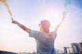 Male teenager holding colorful smoke sticks up in the air over urban city background. Royalty Free Stock Photo