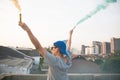 Male teenager holding colorful smoke sticks up in the air over urban city background. Royalty Free Stock Photo