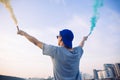 Male teenager holding colorful smoke sticks up in the air over urban city background Royalty Free Stock Photo