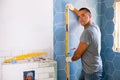 Male tiler laying textured hexagon tiles on bathroom wall, checking level with tool