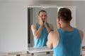 Male touching his beard and face. Sleepy man in bathroom looks at himself in mirror. Morning routine