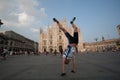 Male tourist cyclist funny posing on handstand on the background of the Duomo di Milano on a sunny summer day in the crowd square