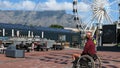 Male Tourist with face mask Table Mountain and big ferris wheel, man in wheelchair