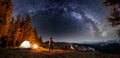 Male tourist have a rest in his camp near the forest at night under beautiful night sky full of stars and milky way Royalty Free Stock Photo