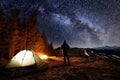 Male tourist have a rest in his camp near the forest at night under beautiful night sky full of stars and milky way Royalty Free Stock Photo