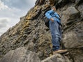 Male tourist in a mountains, look up angle of view. Rough stone wall behind the man. Dangerous risky conditions. Outdoor activity