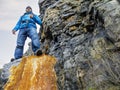 Male tourist in a mountains on orange rock, look up angle of view. Rough stone wall behind the man. Dangerous risky conditions.