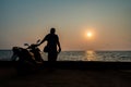 A male tourist parks his motorcycle and stands watching the sunrise over the sea Royalty Free Stock Photo