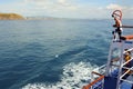 A male tourist is sailing across the sea on a passenger boat. Standing on the upper deck and smiling