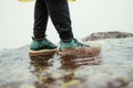 Male tourist standing on a puddle on a rock on a background of misty views, photo of feet in green boots in the water