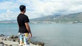 Male tourist standing on rock and enjoying ocean. Concept. Back view of a man standing on a rock cliff and facing the Royalty Free Stock Photo