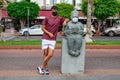 A male tourist wearing a medical face mask poses near a stone sculpture of a masked accordionist on Ataturk Boulevard in Alanya,