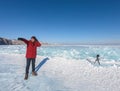 Male tourist in winter coat stands on frozen Baikal lake with ice crystals