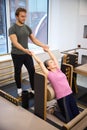 Male trainer helping adult woman doing exercise for back in rehabilitation gym Royalty Free Stock Photo