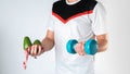 A male trainer holds a dumbbell, avocado and measuring tape for a healthy lifestyle