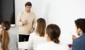 Middle-aged male teacher near interactive board explaining rules to group of students in classroom. Concept of studying Royalty Free Stock Photo