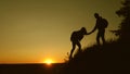 Male traveler holds the hand of a female traveler helping to climb the top of the hill. Tourists climb the mountain at Royalty Free Stock Photo