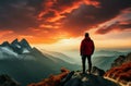 A male traveler in a red jacket stands against the backdrop of a mountain landscape and sunset. View from the back. Tourism, Royalty Free Stock Photo