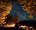 Male traveler showing starry sky to girlfriend in mountains near fire. Royalty Free Stock Photo