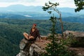 A male traveler is sitting on a rock with a bird`s-eye view of the forest. The concept of recreation and tourism. A man traveler Royalty Free Stock Photo