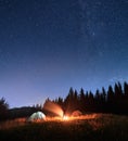 Male traveler standing near campfire and pointing at stars.