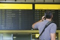 Male Traveler Using Cellphone By Flight Status Board