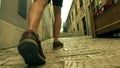 Male traveller`s feet, back view. Walking along ancient Mediterranian city street