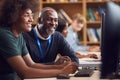 Male University Or College Student Working At Computer In Library Being Helped By Tutor Royalty Free Stock Photo