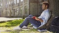 Male university student sitting under tree, reading book, memorizing information