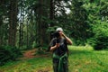 A male videographer with a camera on a stabilizer stands in the woods against a background of trees and adjusts the technique for