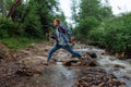 Male videographer jumps over a mountain river with a camera on a stabilizer in his hands. Guy creates video content on a mountain