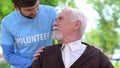 Male volunteer smiling to senior pensioner, social worker support, charity
