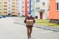 A male volunteer wearing a protective mask walks down the street with a box of groceries, charity