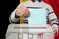 Male voter drops a ballot in a transparent ballot box on the background of the national flag of the country of Belgium, concept of